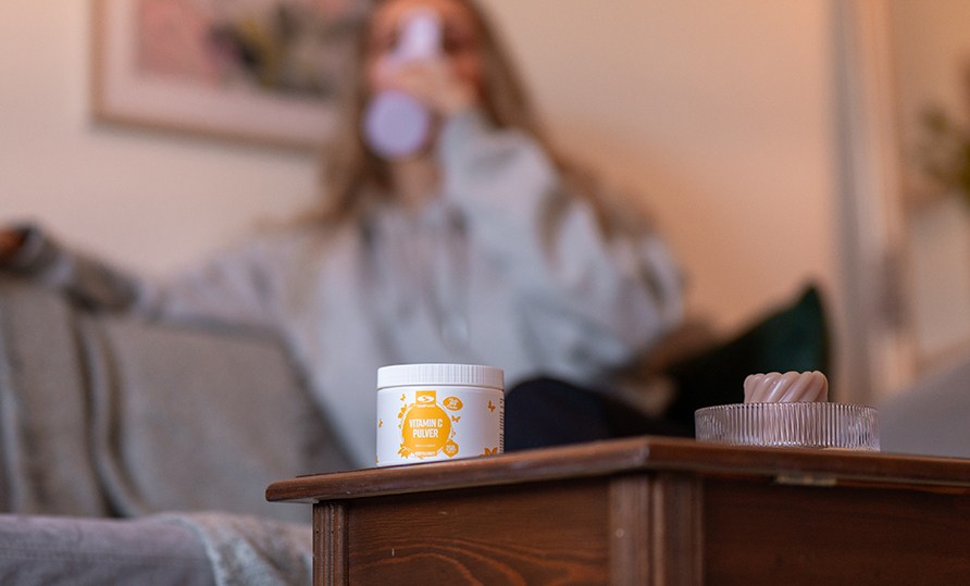 Healthwell C-vitamin pulver str p et bord med en kvinde i baggrunden.